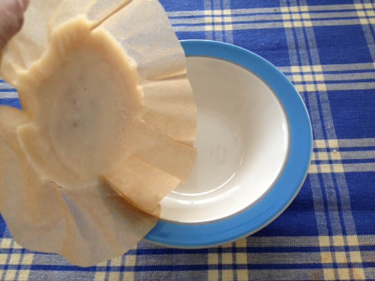 Lifting the hardened bacon grease on parchment paper from the bowl to discard.