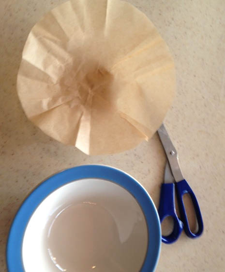 Cutting parchment with scissors to fit a blue bowl for bacon grease.
