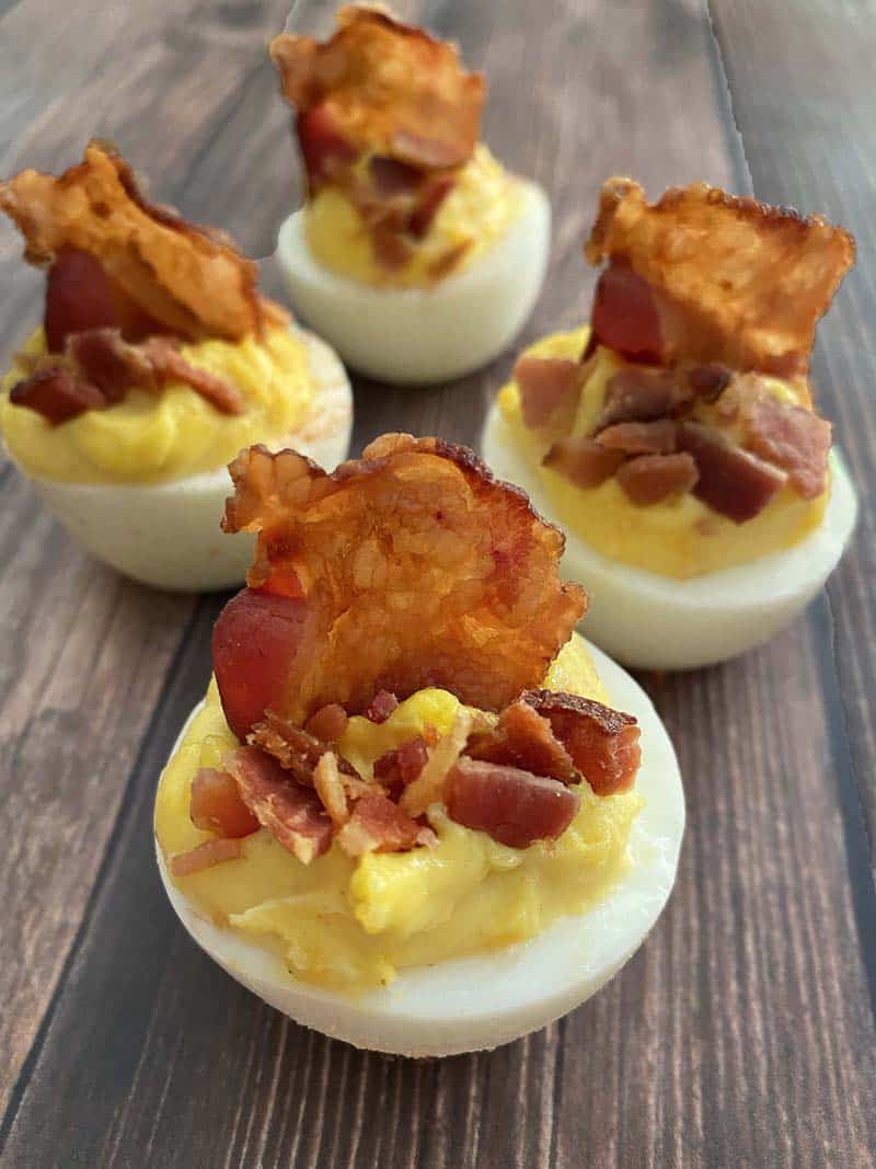 Four deviled eggs with bacon on a wooden background.