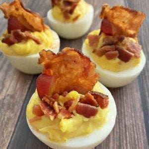 four deviled eggs with bacon on a wooden background