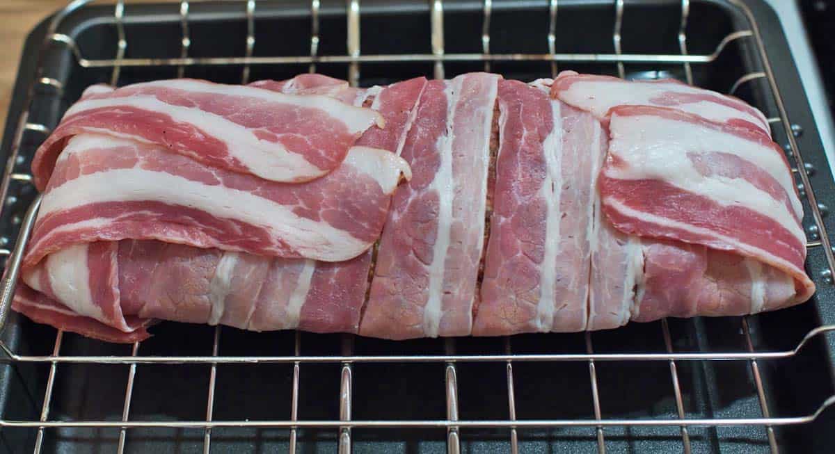 A bacon wrapped pork roast inside of a metal grill basket.