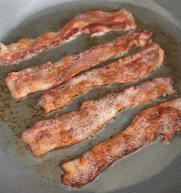 5 strips of bacon cooking in a skillet for Irish burgers.