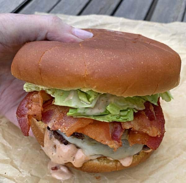 A hand holding a just-cooked Irish Bacon Cheeseburger.