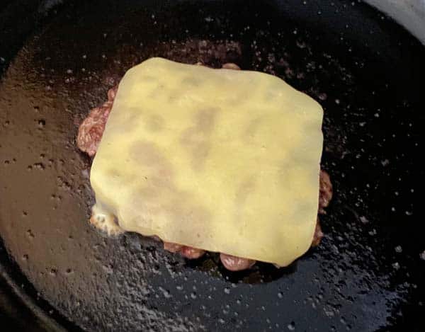 Irish cheddar slice on a hamburger patty cooking in a cast iron skillet.