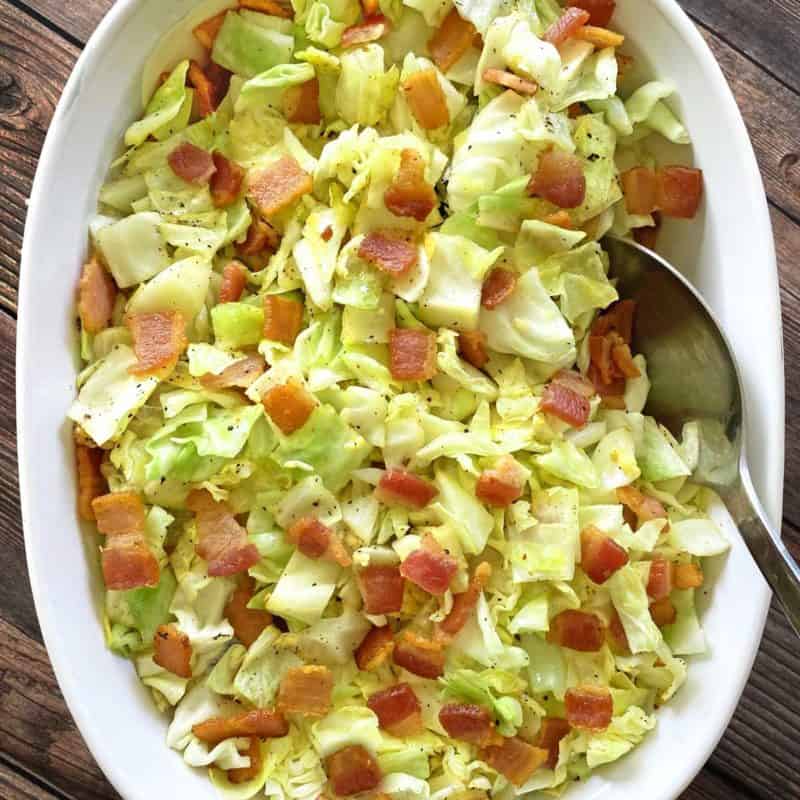 close up of serving dish with fried cabbage with bacon and serving spoon
