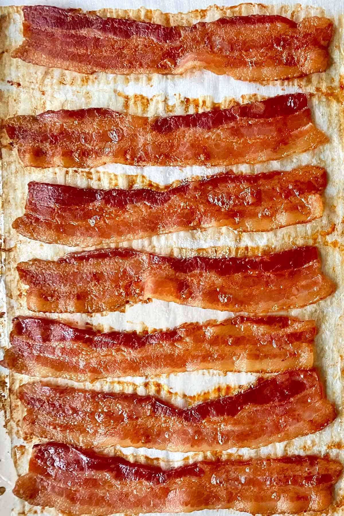 Seven strips of golden brown bacon cooked on an oven baking rack.
