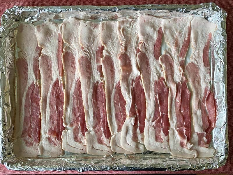 9 strips of bacon arranged in a foil and parchment paper lined baking pan.