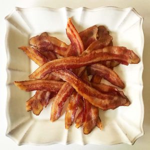 A dozen oven-cooked bacon strips on a cream stoneware fluted square plate.