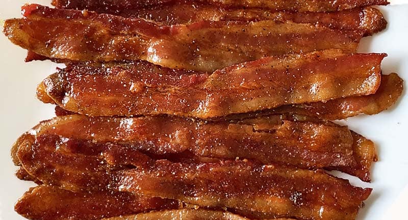 Twelve slices of maple candied bacon arranged in a pile.