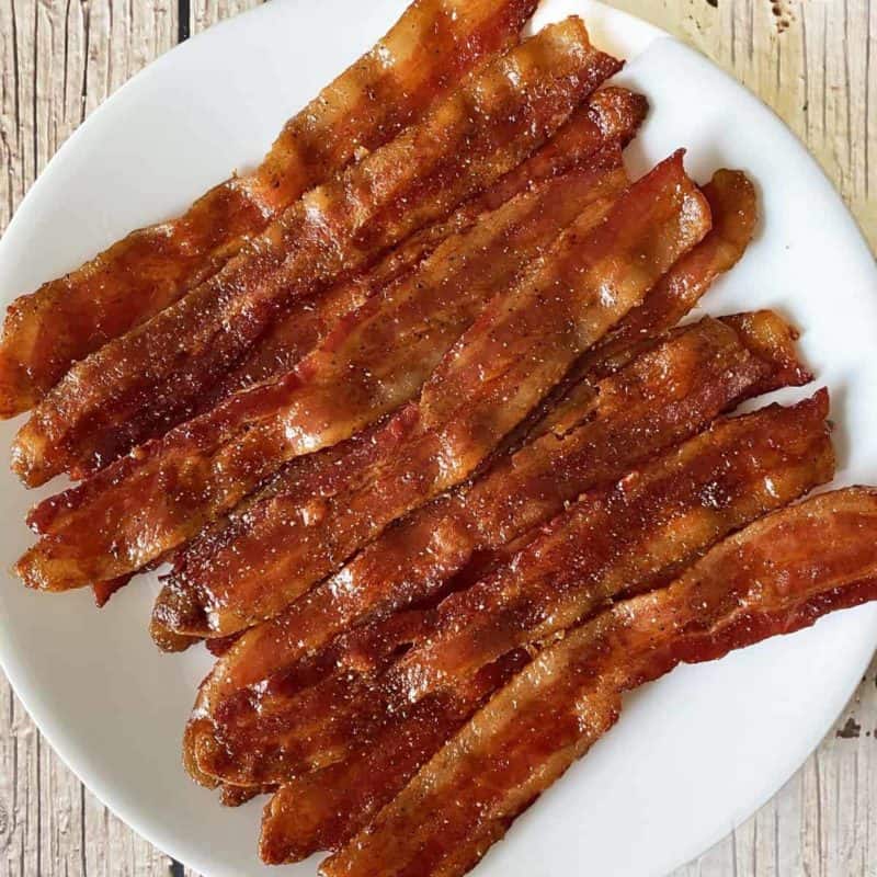 maple candied bacon on a white plate against a weathered wood background.