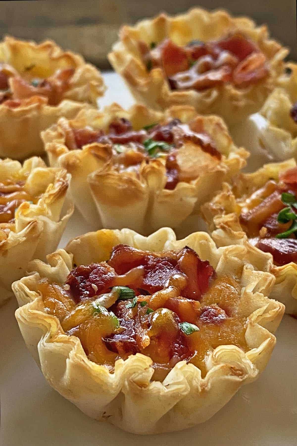Close up of 7 cheese and bacon mini quiches on a white plate.