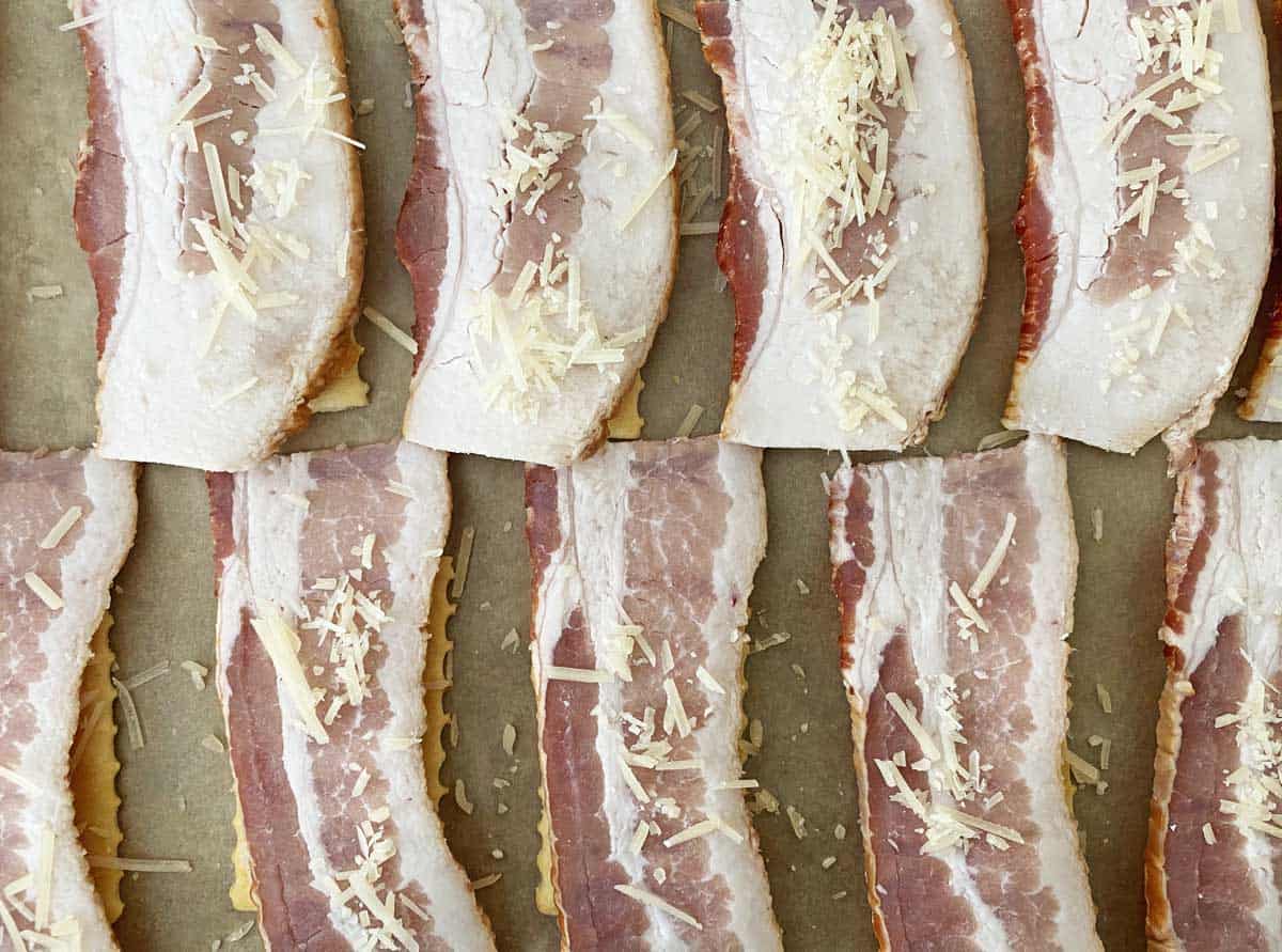 Uncooked bacon crackers sprinkled with parmesan on a parchment lined baking sheet