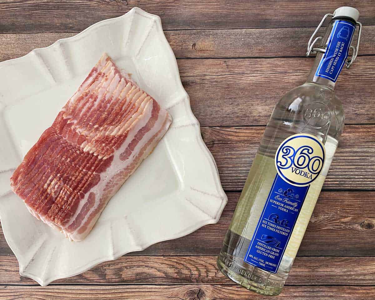One pound of sliced bacon on the left and a 1.75 liter bottle of vodka on the right, against a wood background