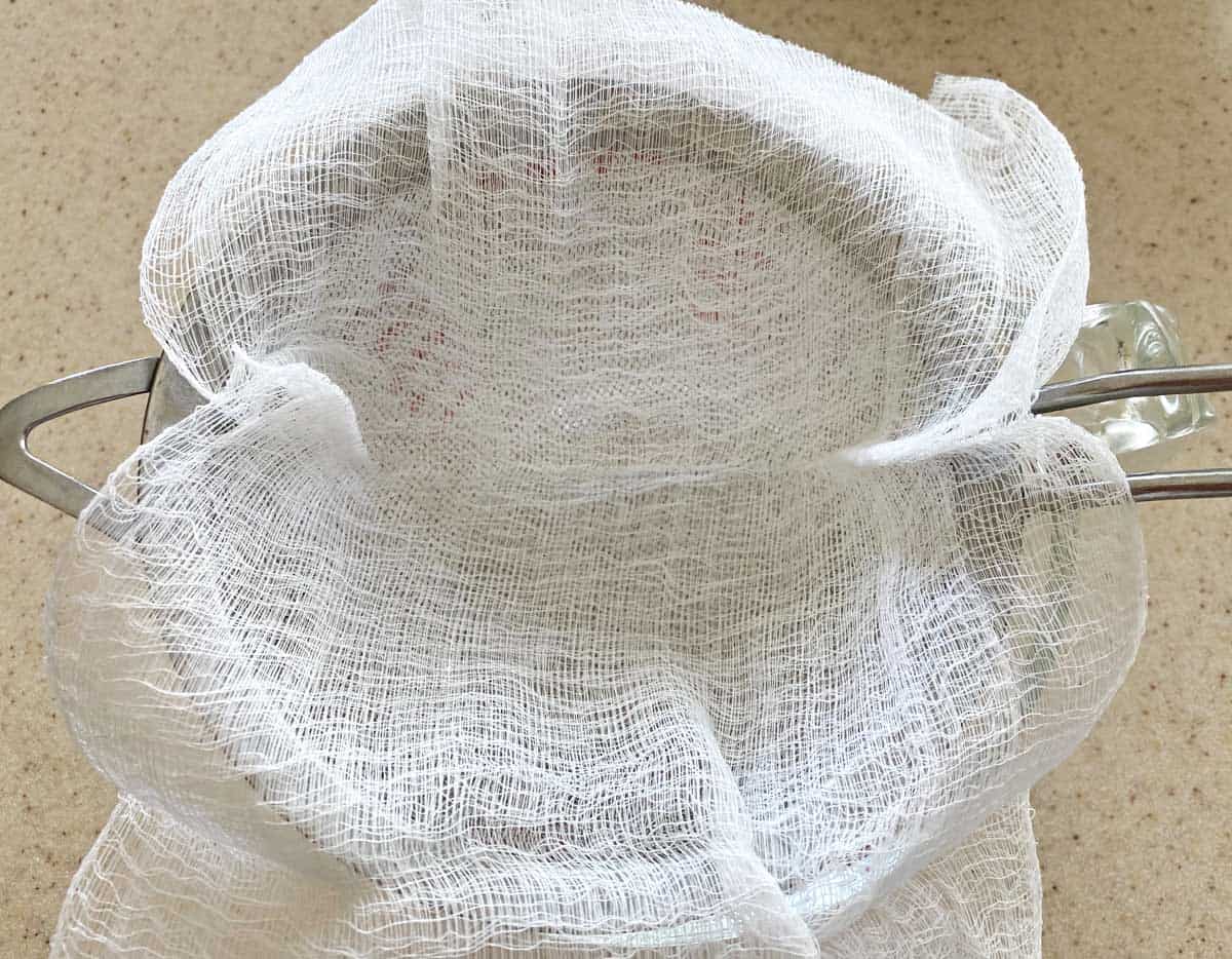 Two layers of cheesecloth inside a strainer which is on top of a large measuring cup. 