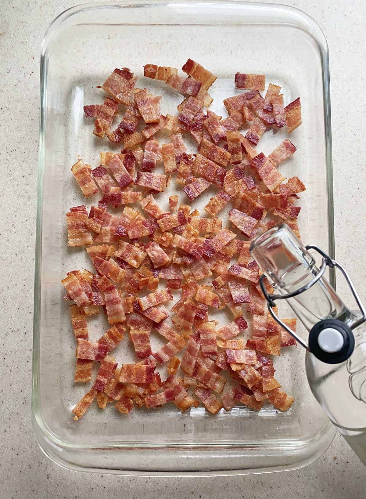 Pouring vodka over chopped cooked bacon in a 9 x 13 inch glass baking dish