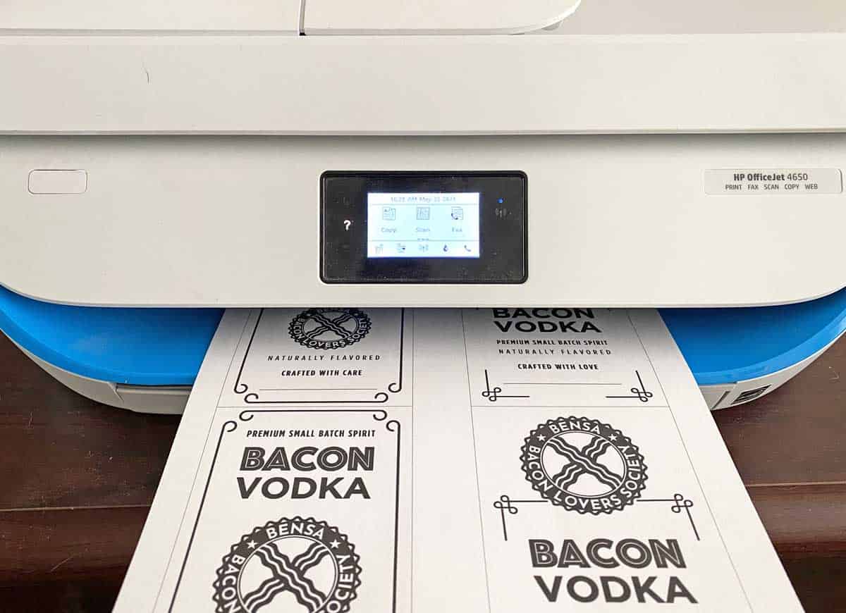 A home laser printer with a sheet of paper printed with four BENSA Bacon Vodka labels. 