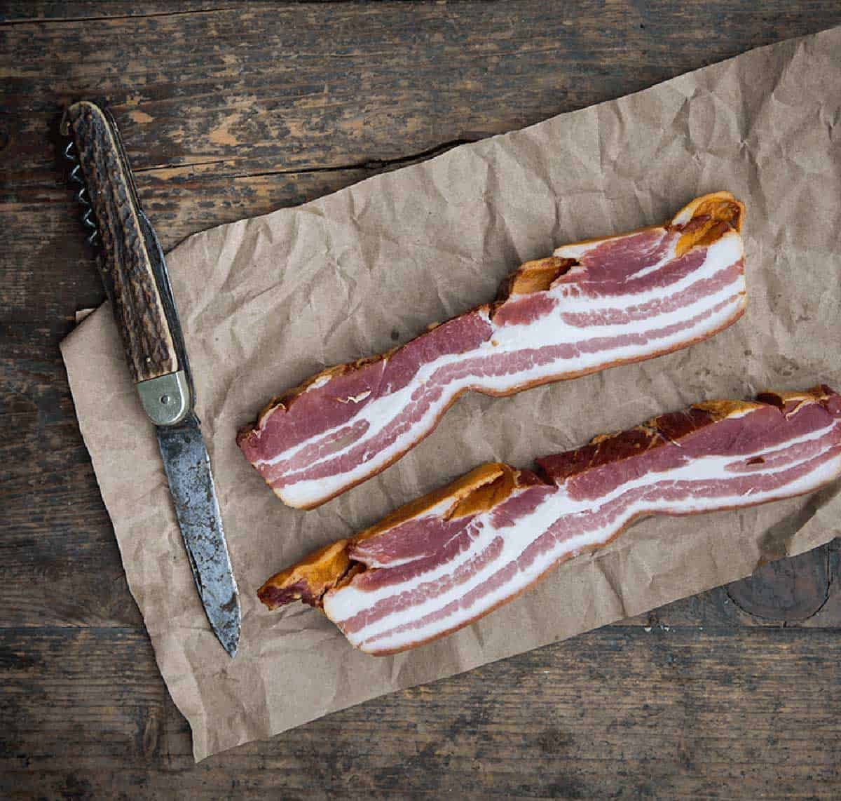 A slab of bacon on butcher paper with a knife.