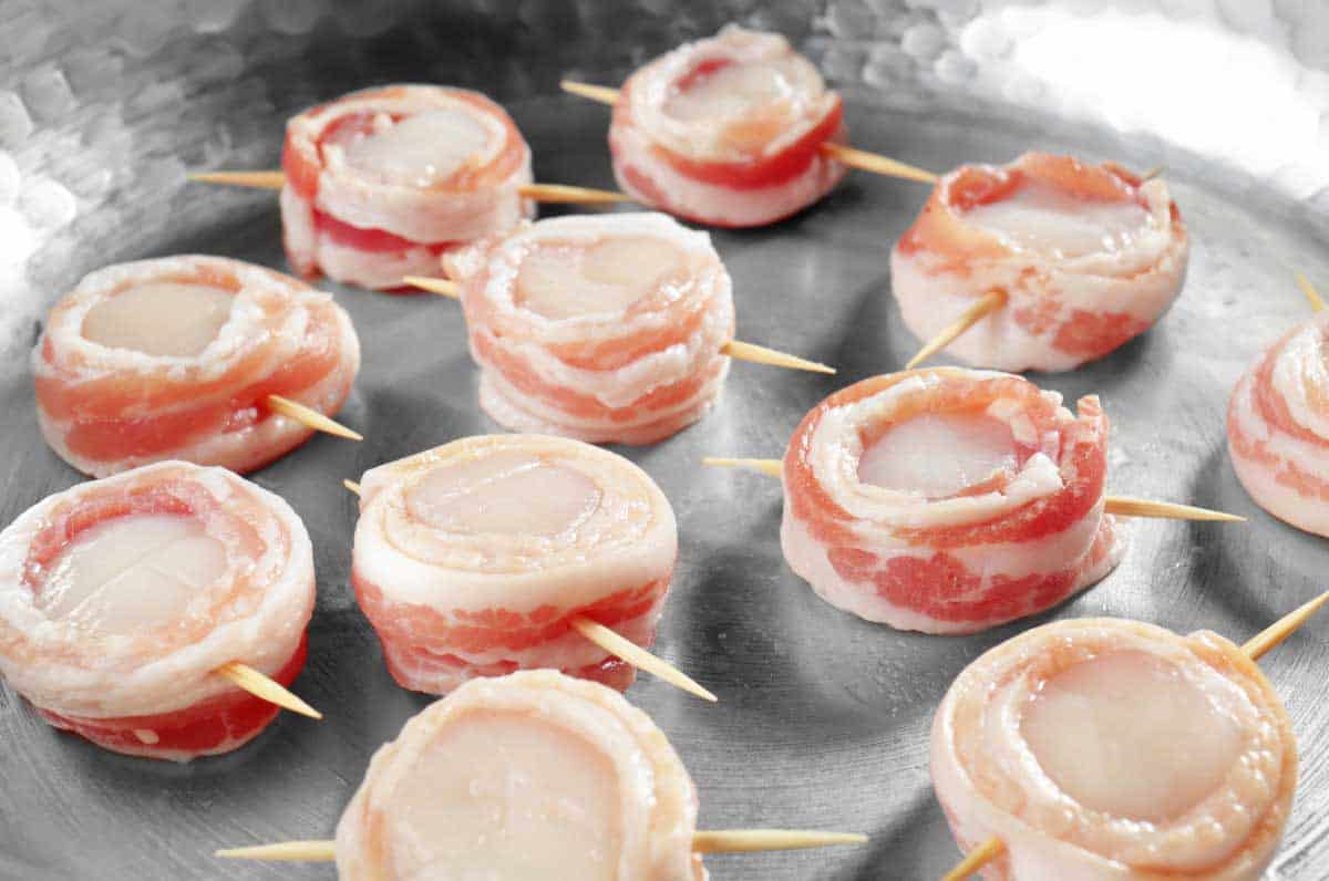 8 raw bacon wrapped scallops in a pan.