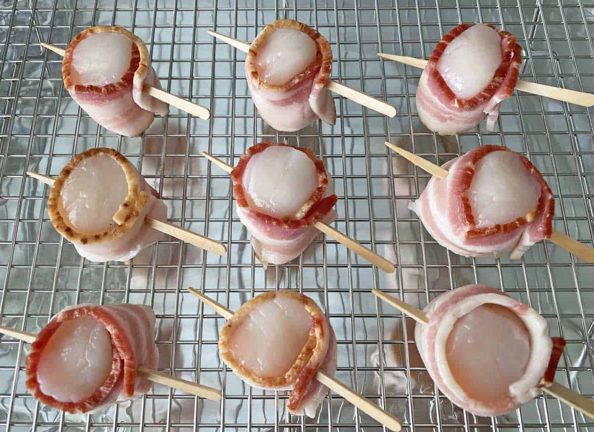 Nine bacon wrapped scallops on a broiler pan.