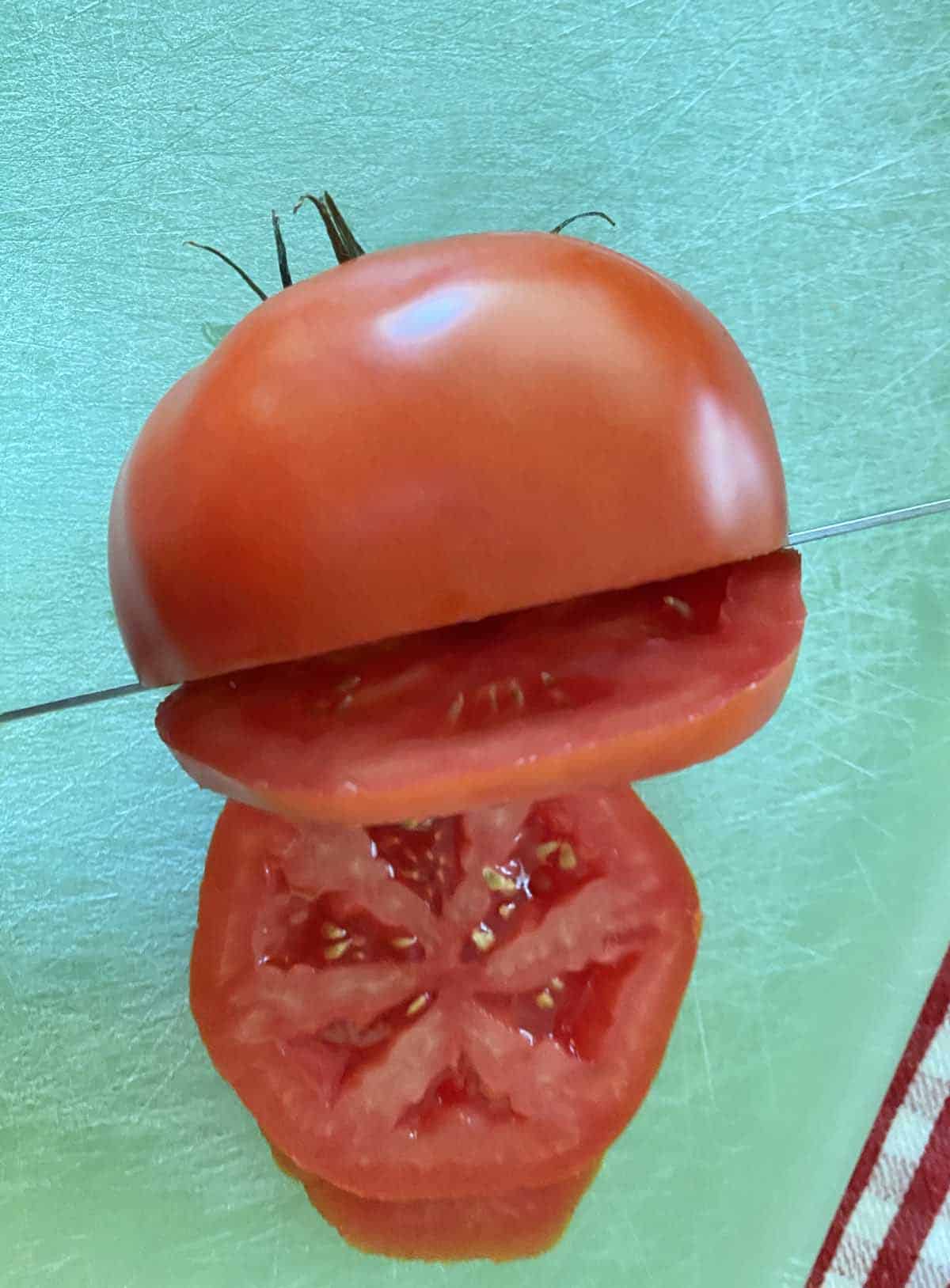 A ripe tomato being sliced by a knife on a green cutting board.
