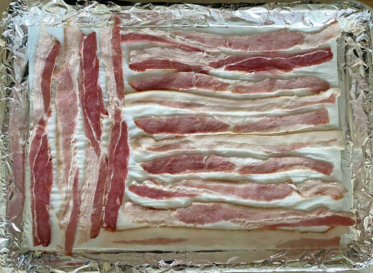 Uncooked bacon on a foil and parchment paper lined baking sheet