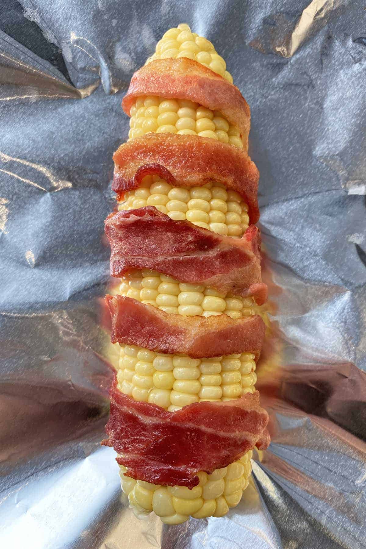 One ear of bacon wrapped corn just prior to being wrapped in foil and grilled