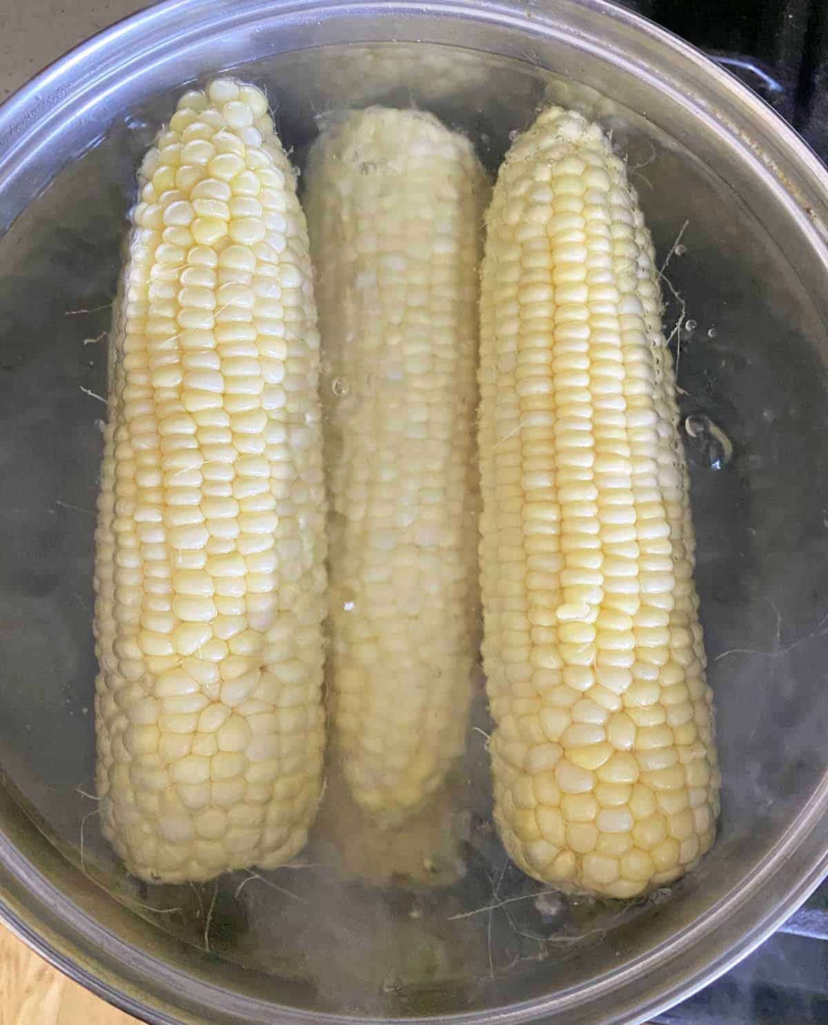 Six ears of corn cooking in a large pot of boiling water