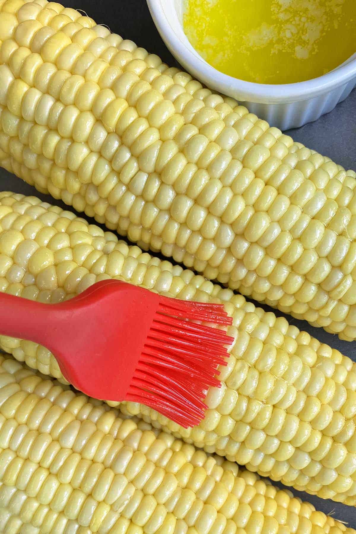 Close up of three ears of corn being brushed with garlic butter