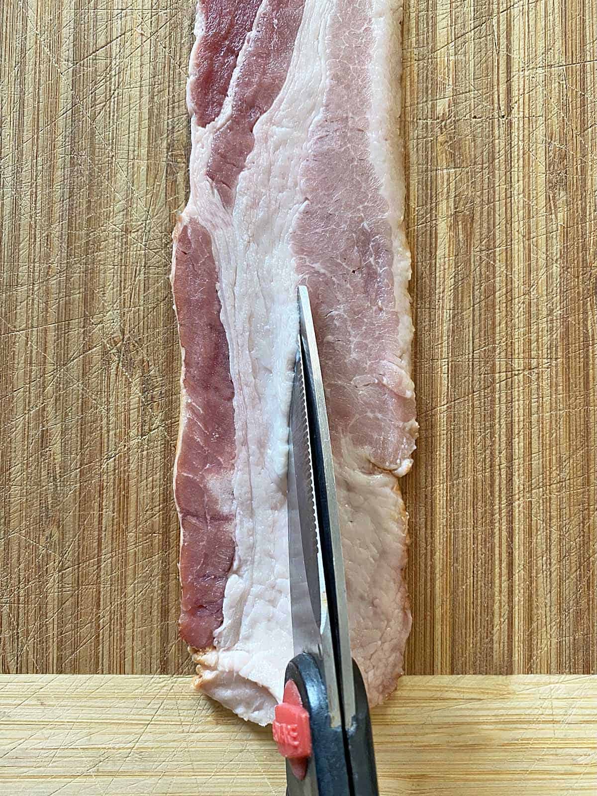 Scissors cutting a piece of bacon lengthwise in a strip