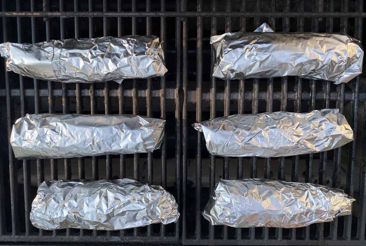 Six ears of foil wrapped corn on a barbecue grill