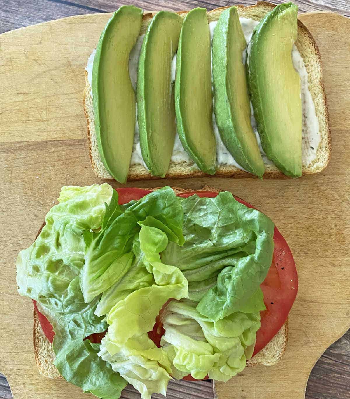 One piece of toast with basil mayonnaise and avocado, and one piece of toast with tomato and lettuce.
