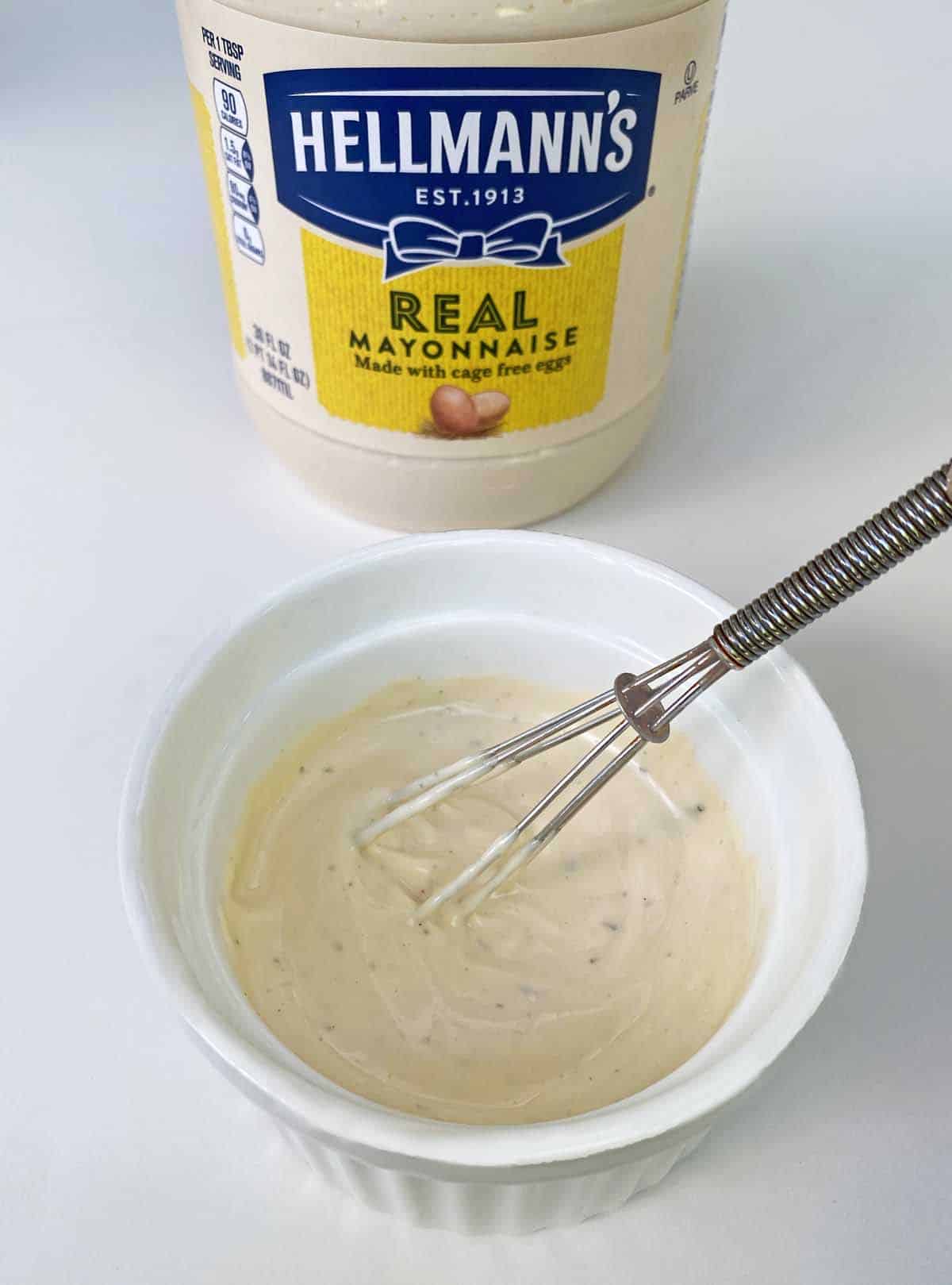 whisking ingredients for ranch balsamic mayo in a small white bowl, with Hellman's mayonnaise behind.