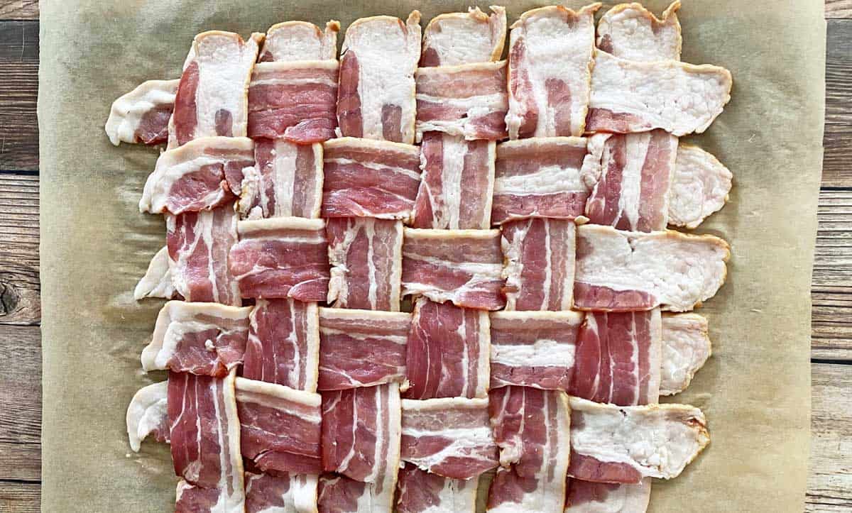 12 strips of bacon woven in a square, on a sheet of parchment paper