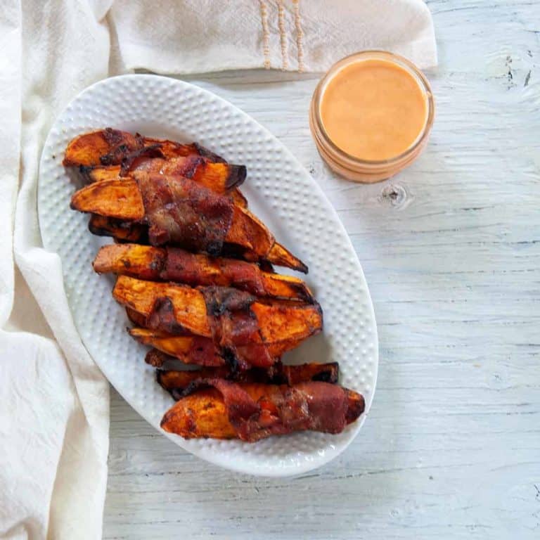 Grilled bacon sweet potato fries on a white serving platter with dipping sauce