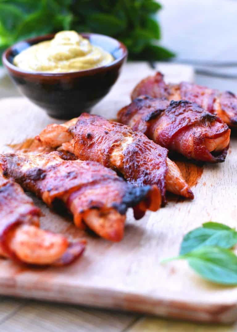 5 pieces of bacon wrapped chicken strips with dipping sauce in a black dish