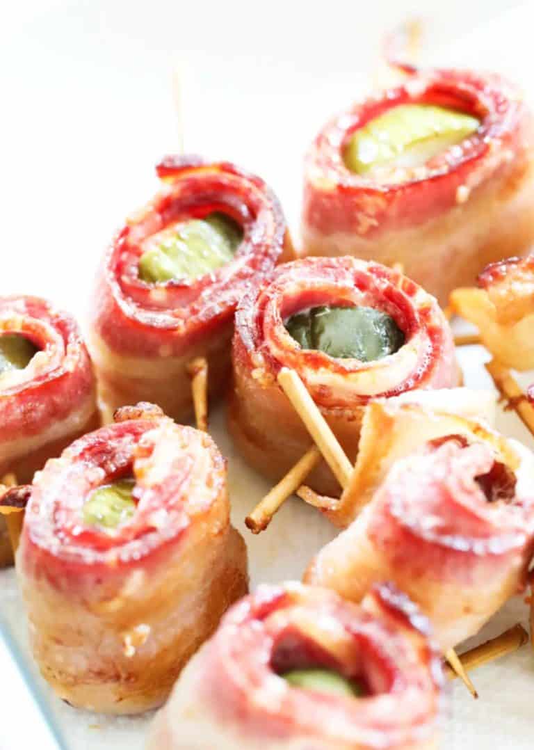 close up of 7 pieces of air fryer bacon wrapped pickles on a white background