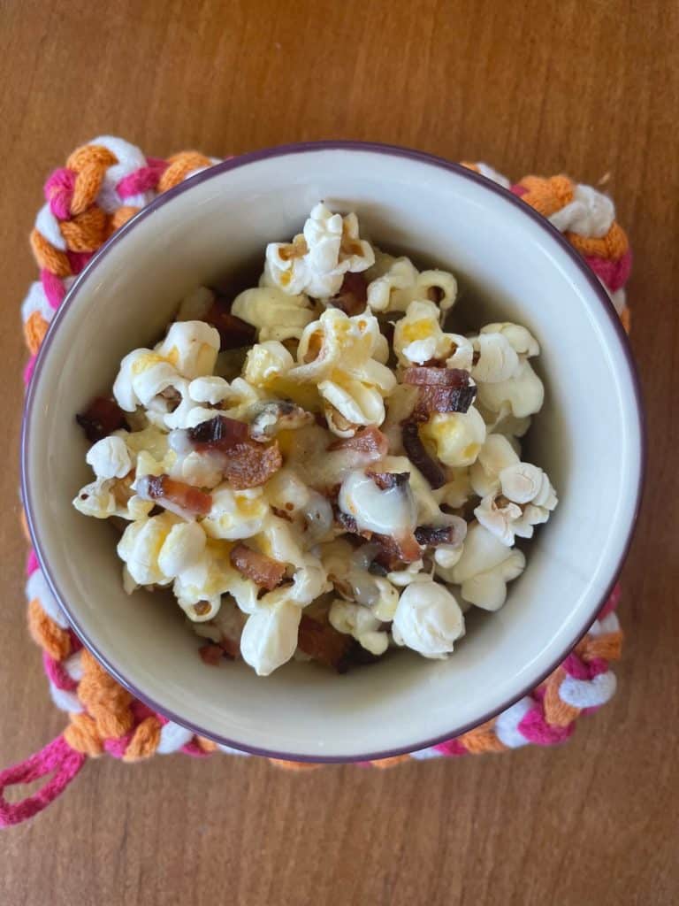 a white bowl with bacon cheddar popcorn on a multicolored potholder