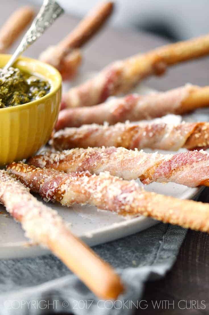 eight bacon wrapped breadsticks on a platter with dipping sauce