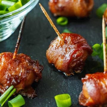 4 bacon wrapped water chestnuts with a small bowl of chopped scallions