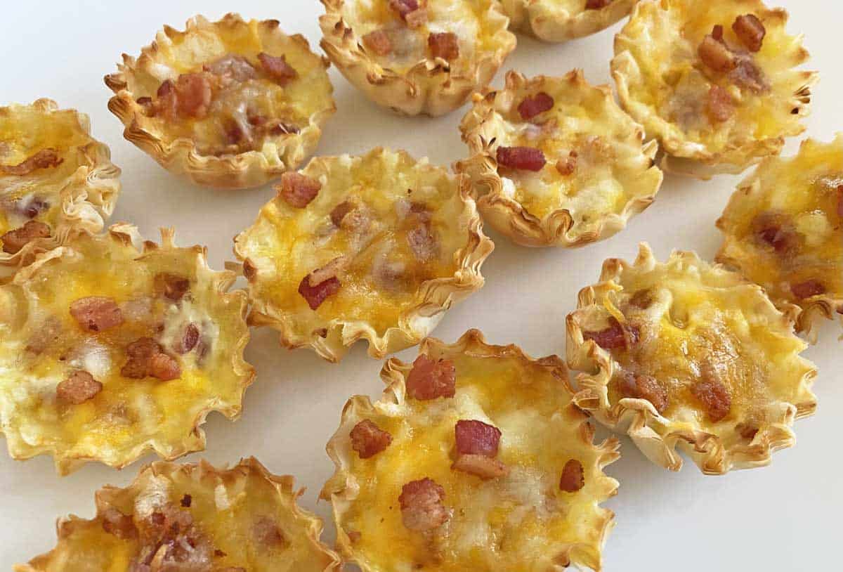 A dozen baked cheese and bacon mini quiches warm from the oven, on a white plate.