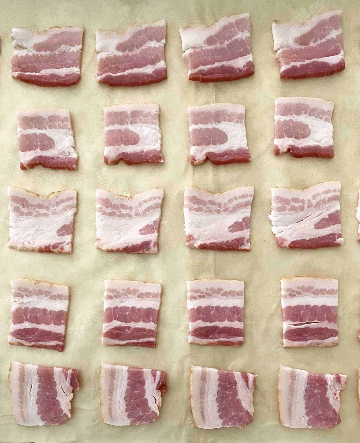 20 small raw bacon squares on a piece of parchment paper