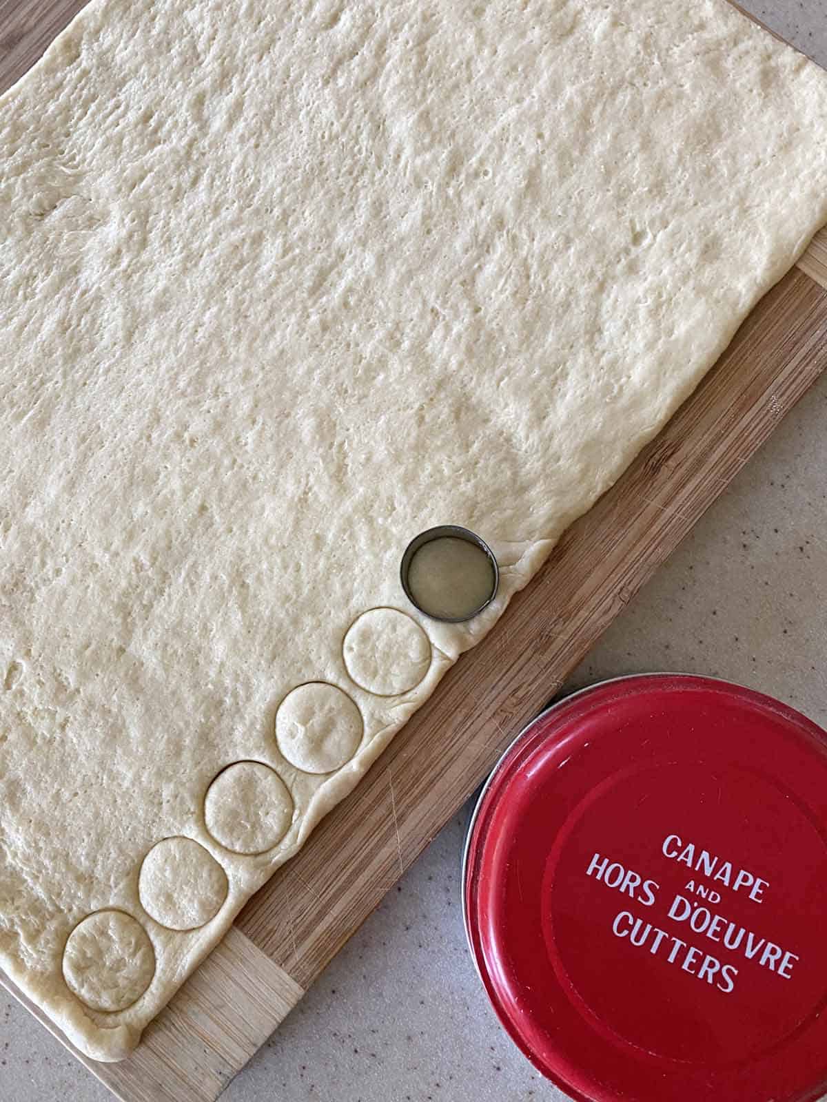 6 round circles cut into crescent dough, with a small red container marked "Canape and Hors D'oeuvre Cutters" in the lower right corner. 