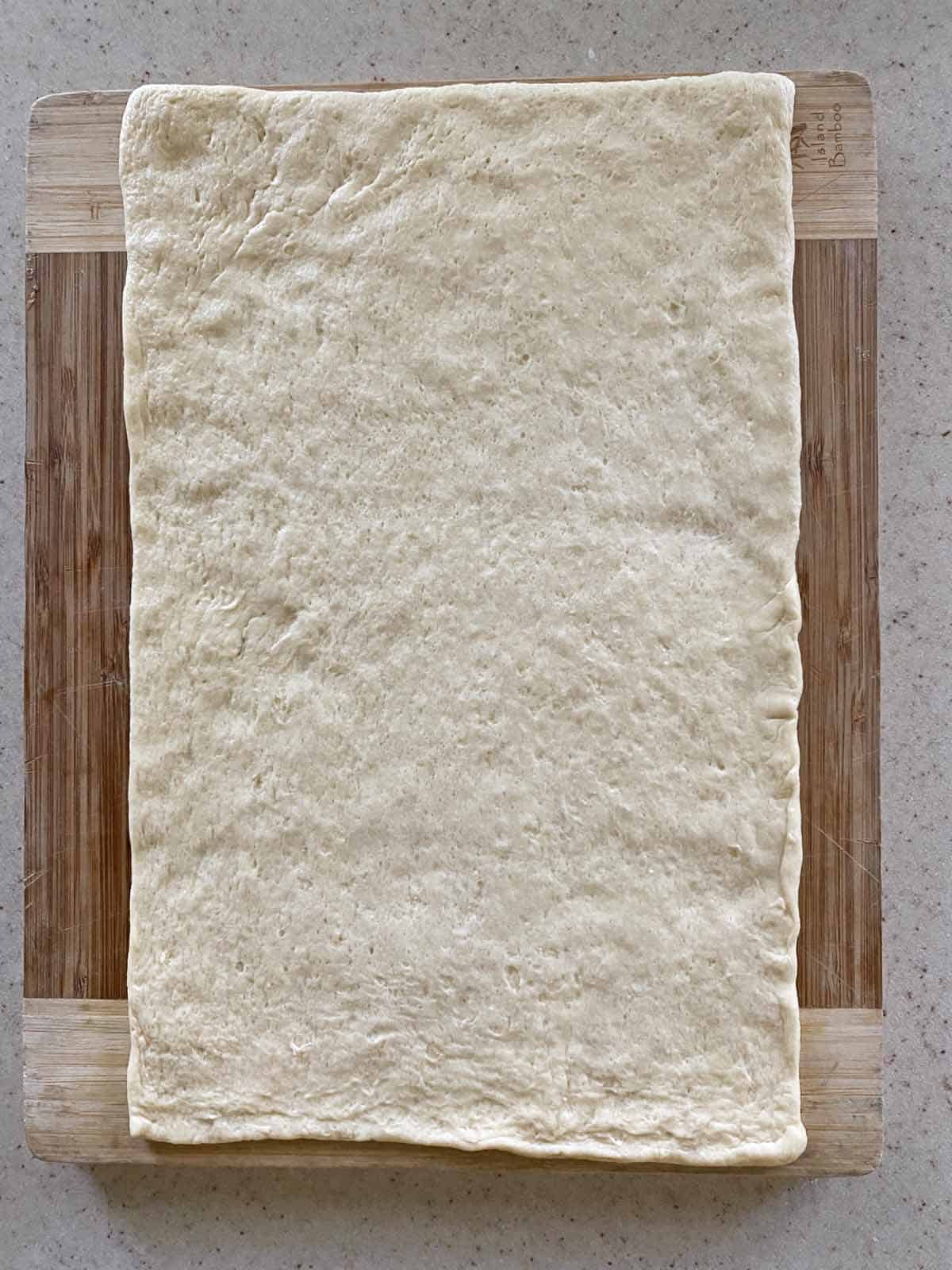 Crescent dough from a tube rolled out and patted on a bamboo cutting board.