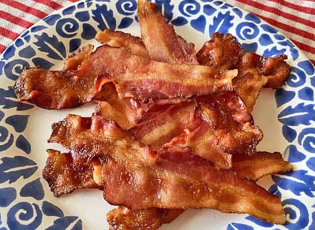 A blue and white plate containing a dozen strips of crispy, oven cooked bacon.