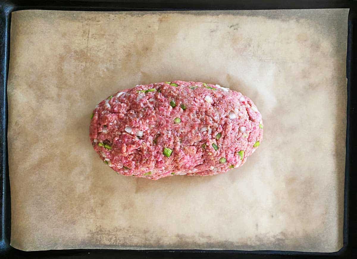 An uncooked meatloaf on a parchment paper lined baking sheet.