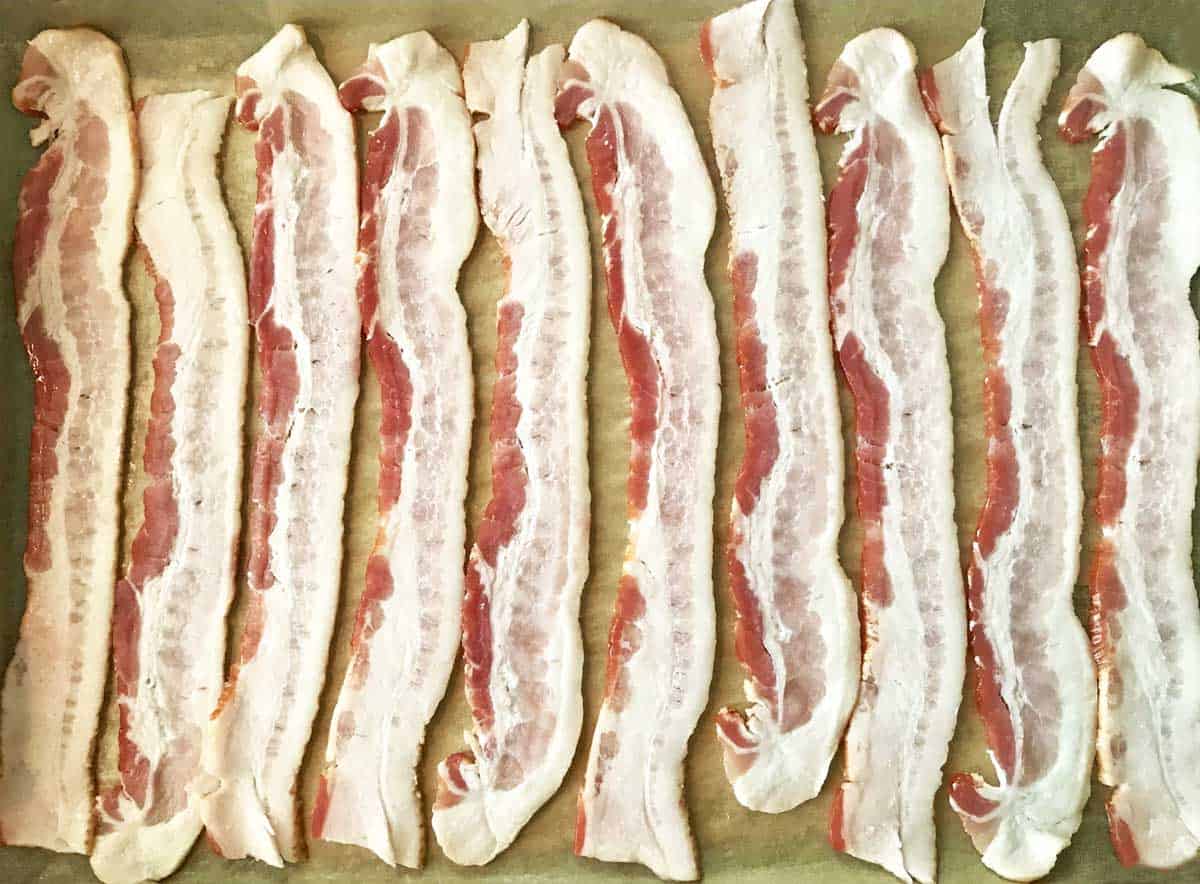 10 strips of bacon arranged on a parchment paper lined baking sheet.