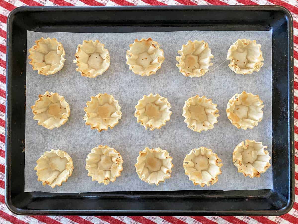 15 unfilled phyllo shells on a parchment-lined baking sheet.