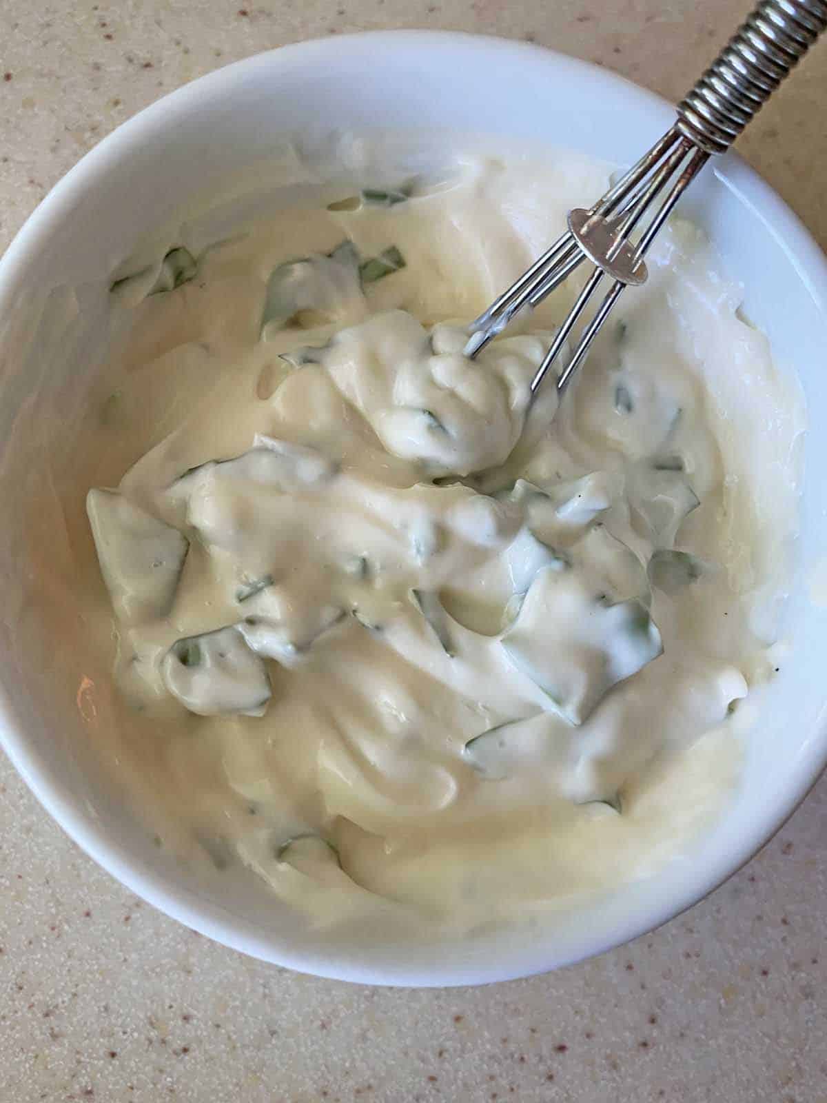 A small white bowl with basil mayonnaise and a small silver whisk to blend the ingredients.