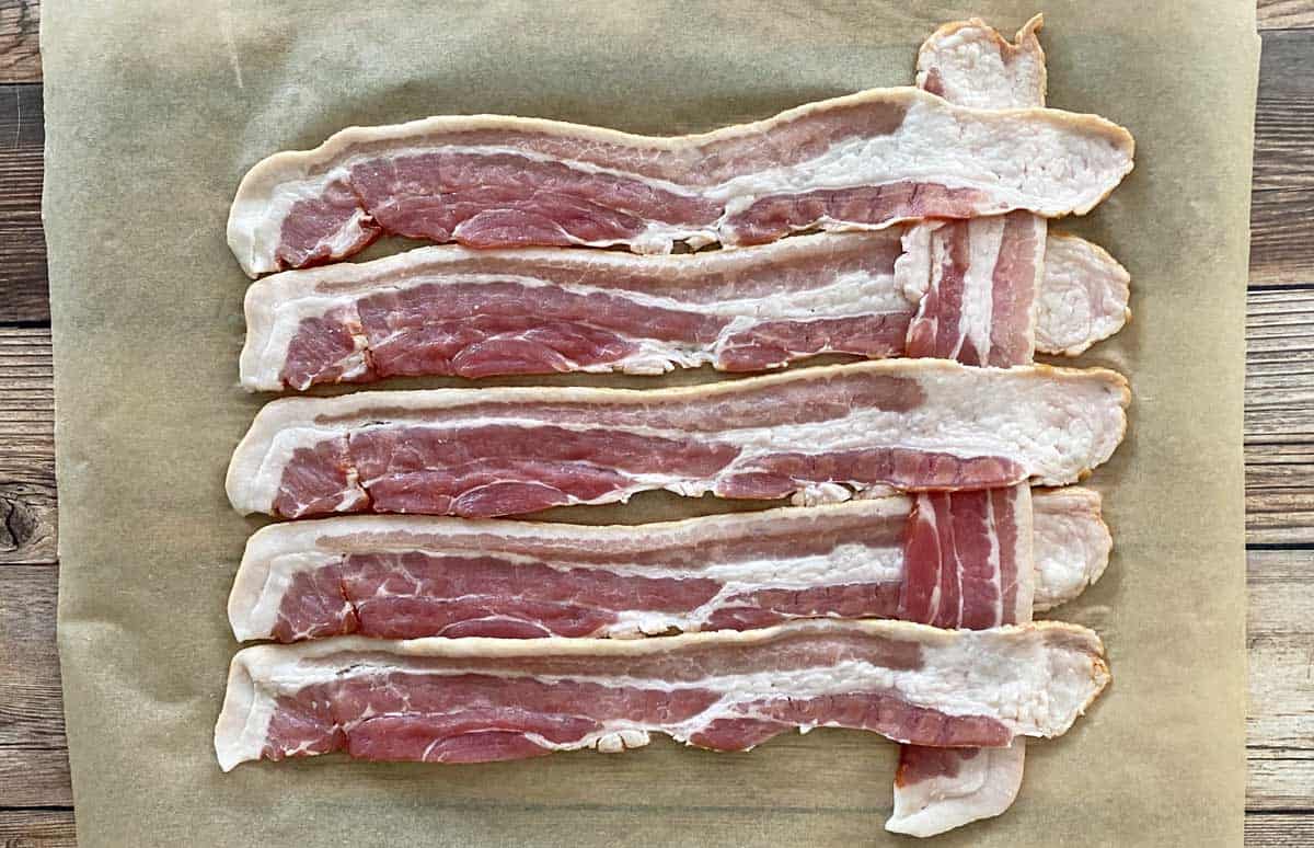 A process photo showing the first step of making a bacon weave, with seven strips of bacon on parchment paper.