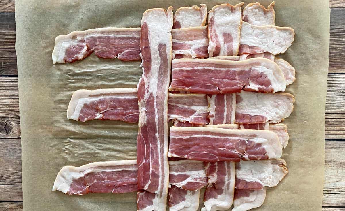 A process shot showing how to make a bacon weave, with half of the bacon slices woven together, on a piece of parchment paper.